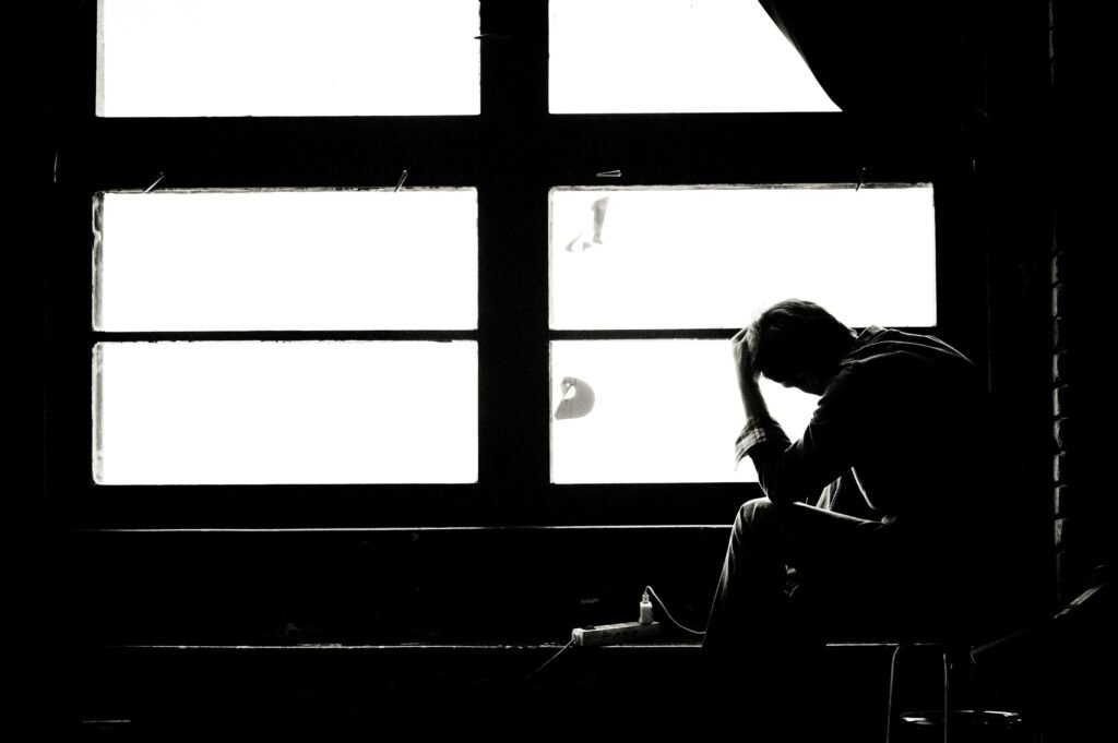 Persona sentada junto a una ventana con la cabeza inclinada, en una escena en blanco y negro