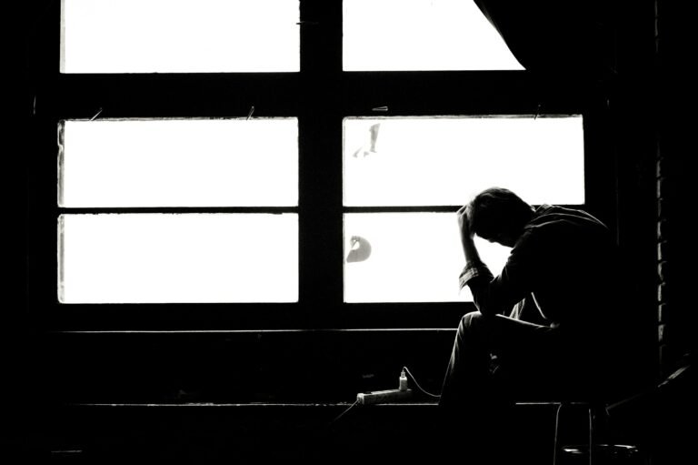 Persona sentada junto a una ventana con la cabeza inclinada, en una escena en blanco y negro